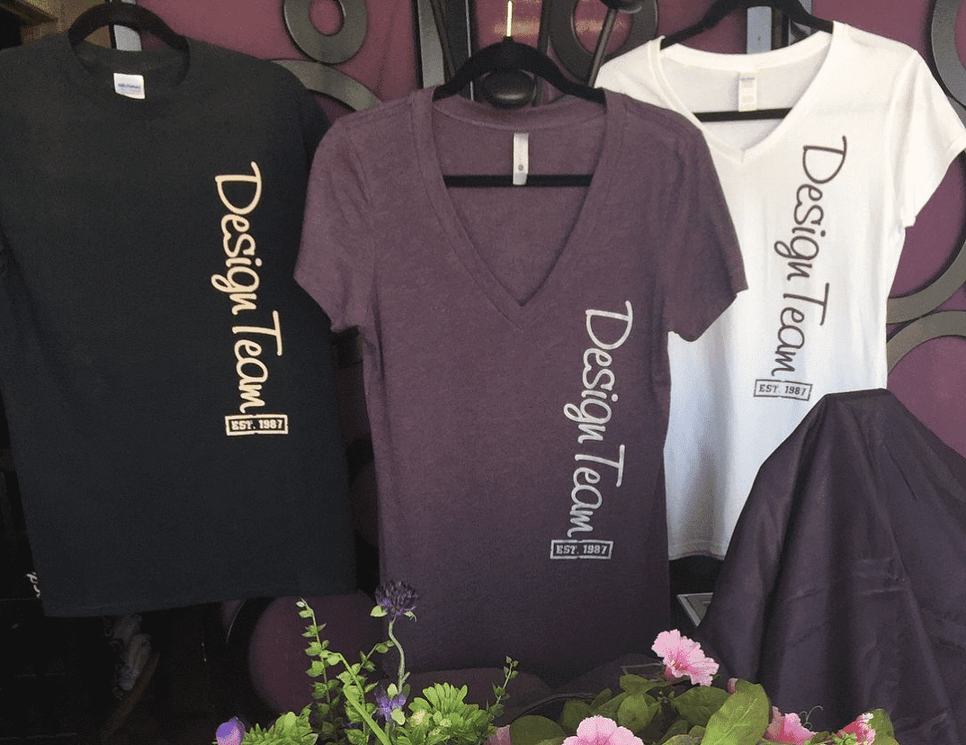 Three t-shirts with "Design Team" logo displayed on hangers.