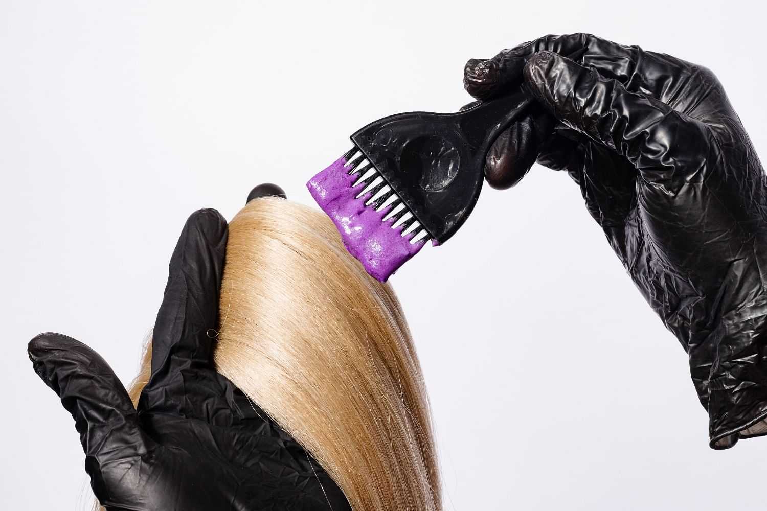 Stylist applying purple dye to blonde hair with a brush.